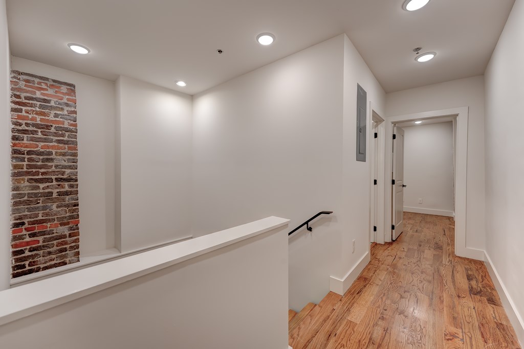 A hallway with a brick wall on the left and wooden floors.