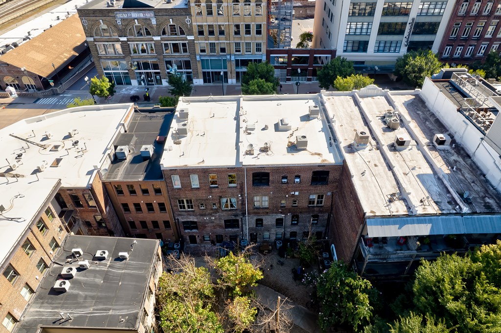 A large, multi-story building with a flat roof is surrounded by other buildings.