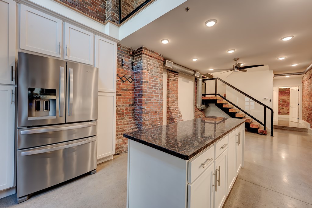 A kitchen with a stainless steel refrigerator and a brick wall.