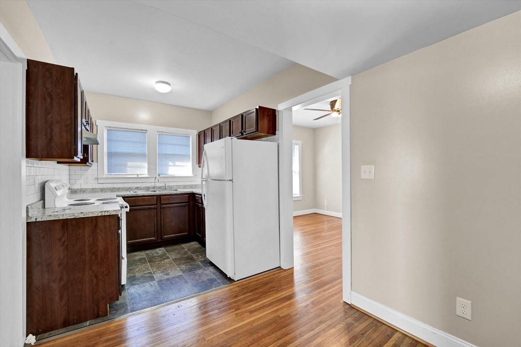 an empty kitchen with white appliances and wood floors