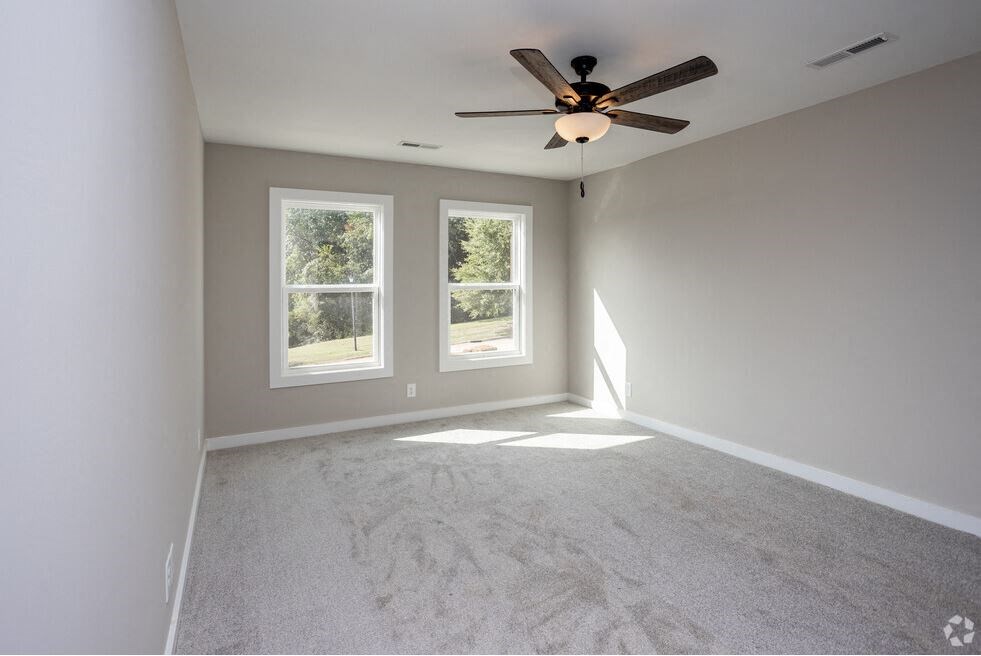 an empty living room with a ceiling fan and two windows
