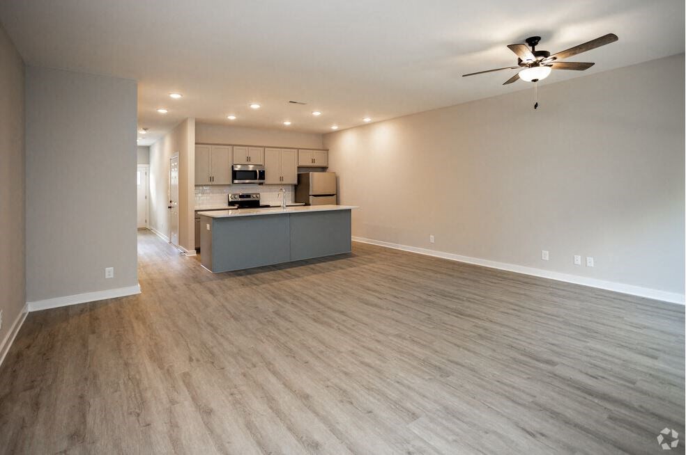 an empty living room with a kitchen and a ceiling fan