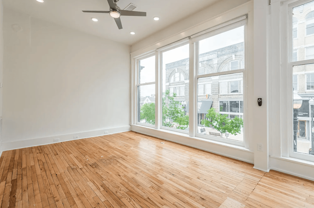 an empty living room with a ceiling fan and large windows
