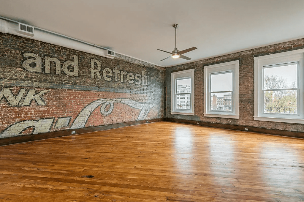 an empty room with wood floors and a brick wall with a mural on it that says and