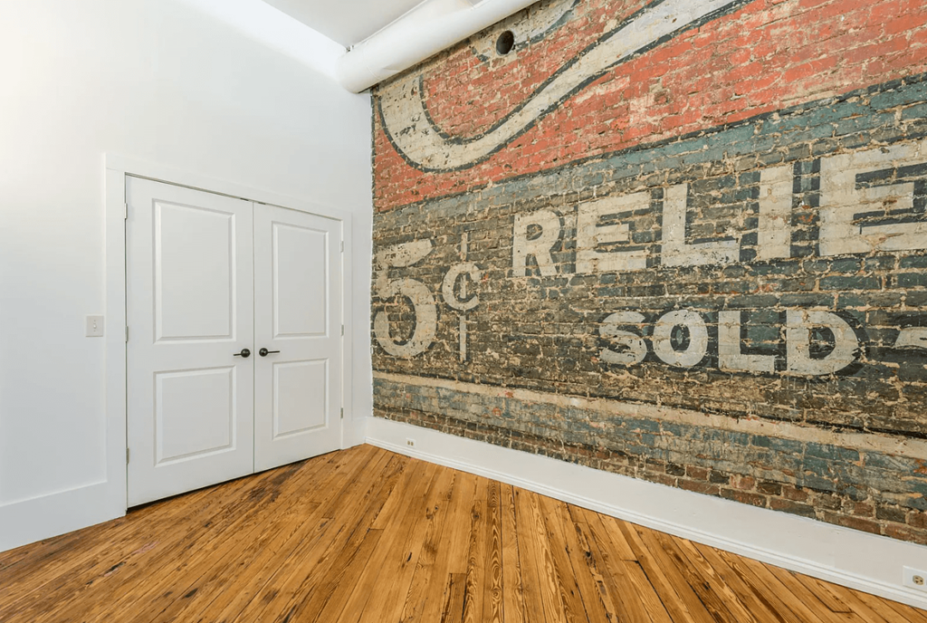 an old sign on a brick wall in a room with wooden floors and a white door