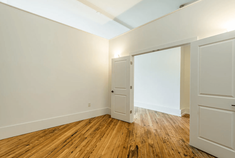 a bedroom with white walls and wood floors and a door