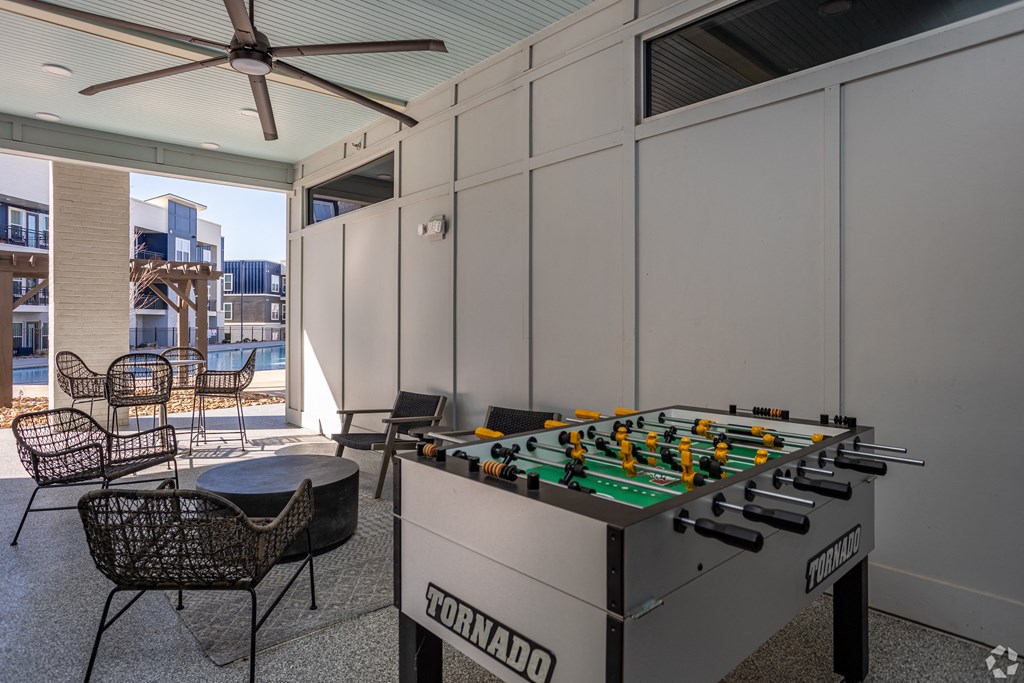 A foosball table is in the middle of a room with a ceiling fan.