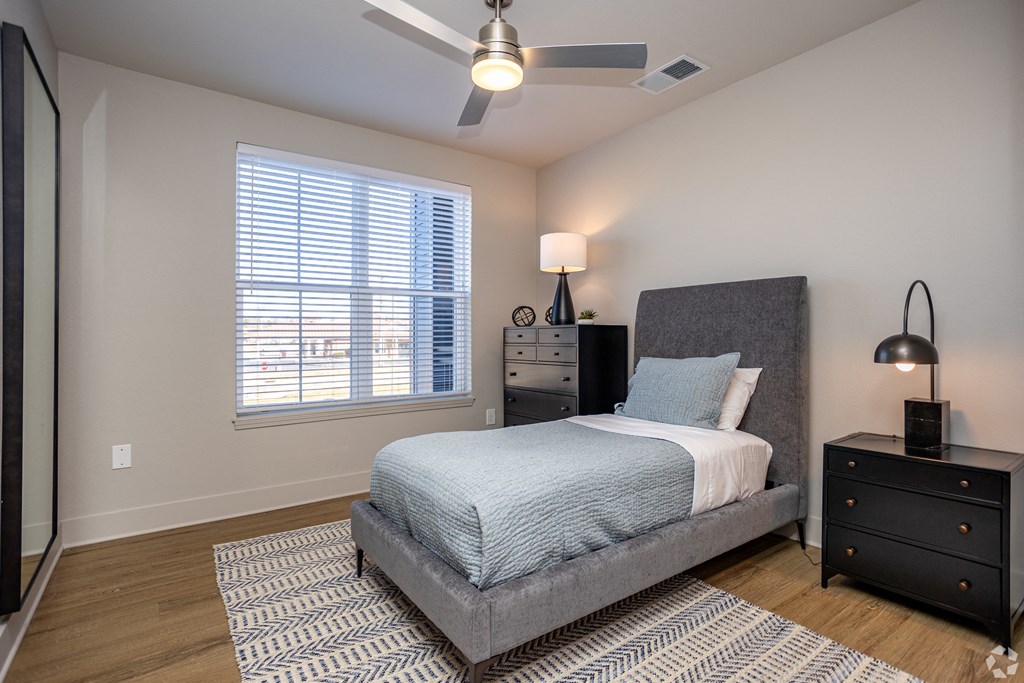 A bedroom with a bed, nightstand, and window with blinds.