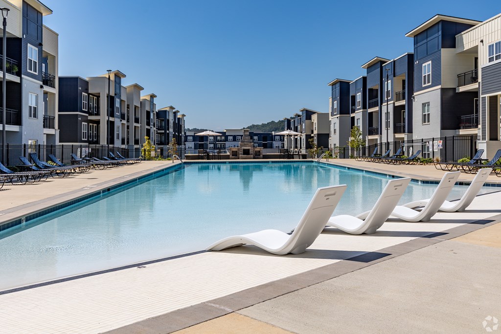 A swimming pool surrounded by sun loungers and apartment buildings.