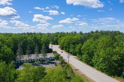 A road stretches through a green forest with a white building on the side.