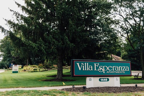 A sign for Villa Esperanza apartments is in front of a large tree.