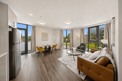 A modern living room with a brown sofa, a coffee table, and a dining table with chairs.