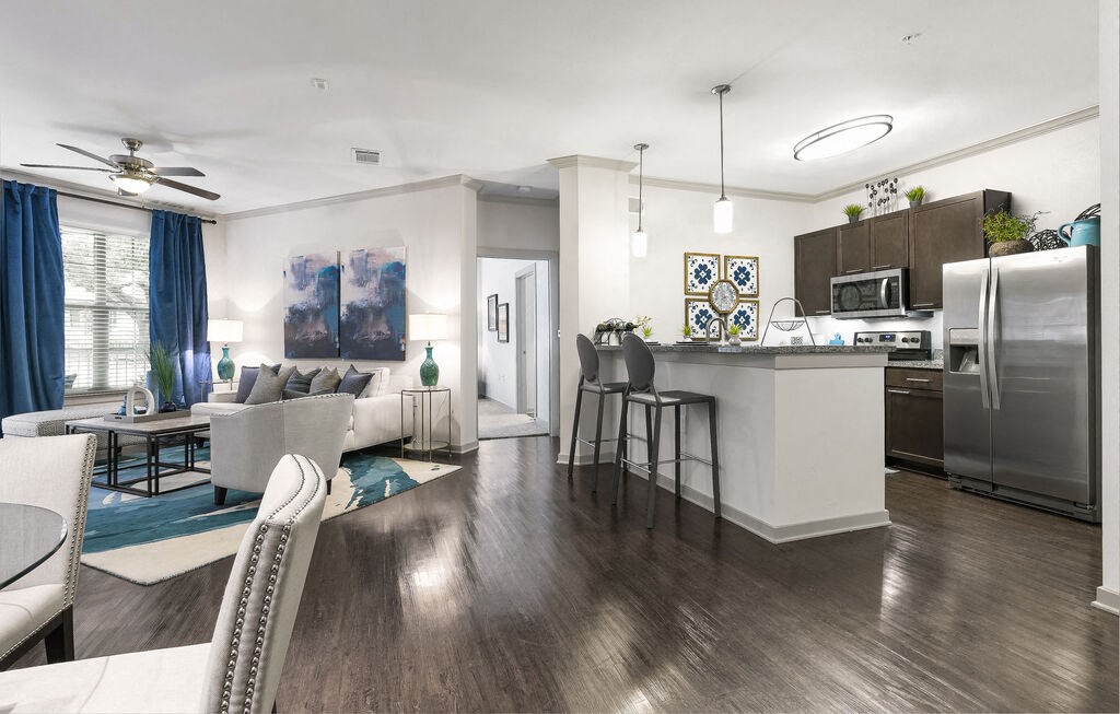 a living room and kitchen area with white walls and wood flooring at 95twenty Apartments, Austin, Texas
