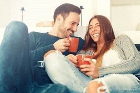 a man and woman sitting on a couch holding cups of coffee