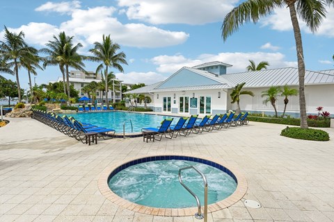 A pool with a hot tub and chairs in front of a white building with a blue roof.