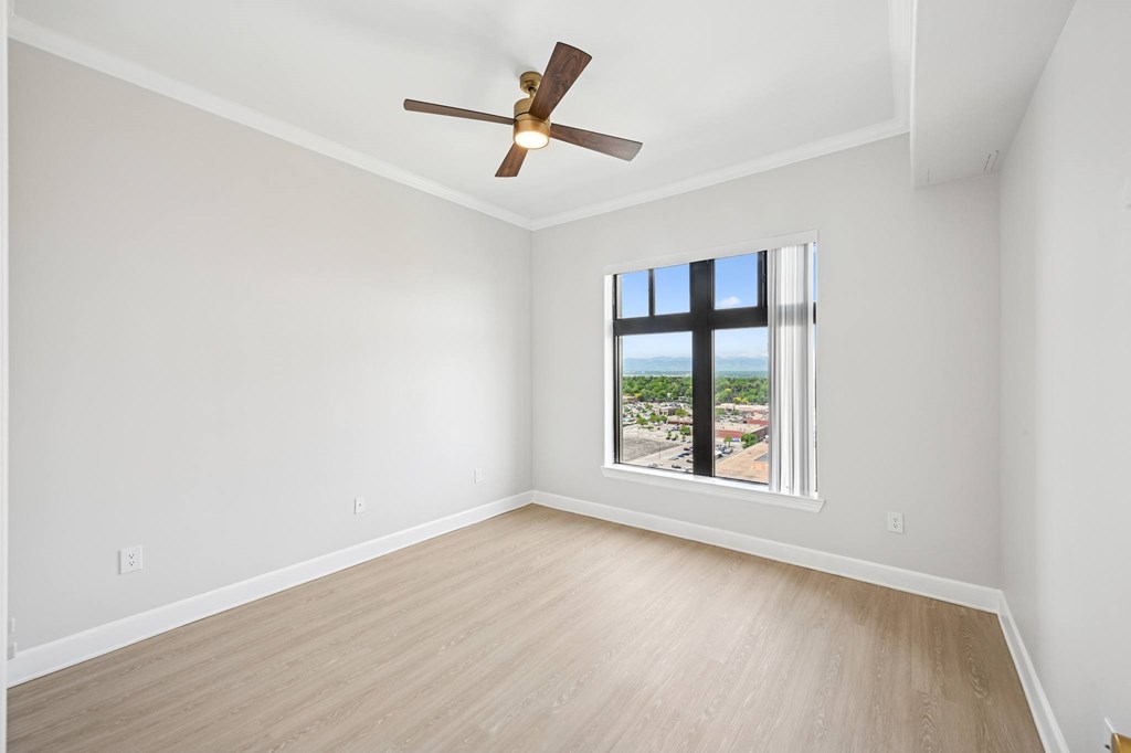 A room with a ceiling fan and a window overlooking a street.