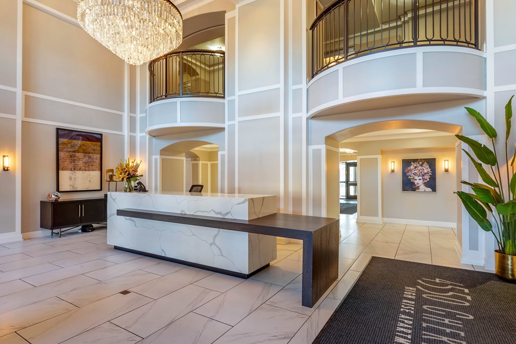 A large, well-lit lobby with a marble reception desk and a chandelier.