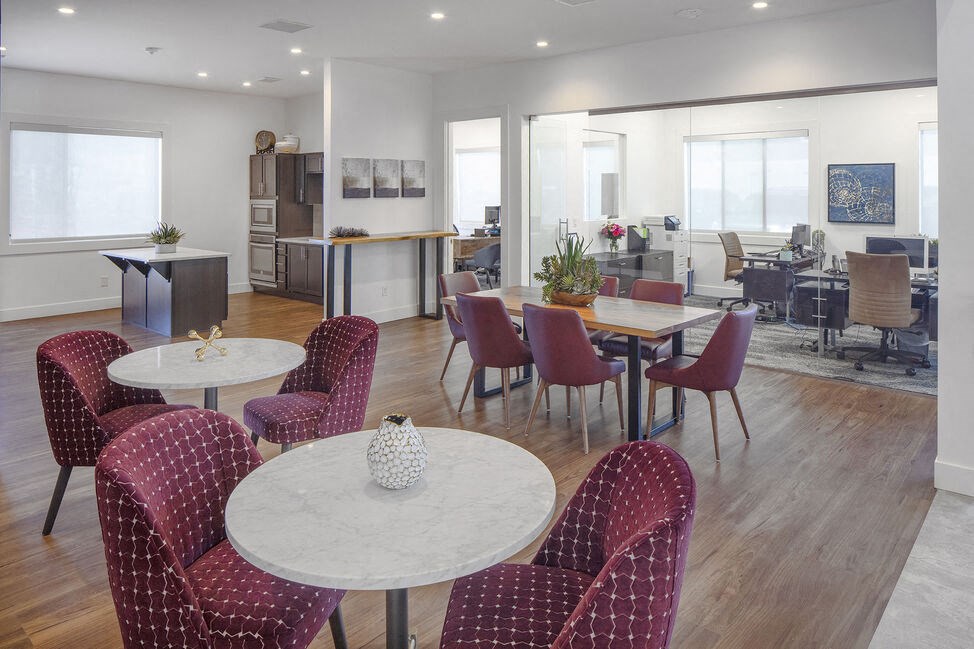 a room with tables and chairs and a kitchen in the background