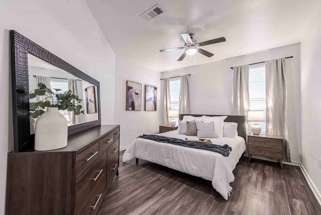 A bedroom with a bed, dresser, mirror, and a ceiling fan.
