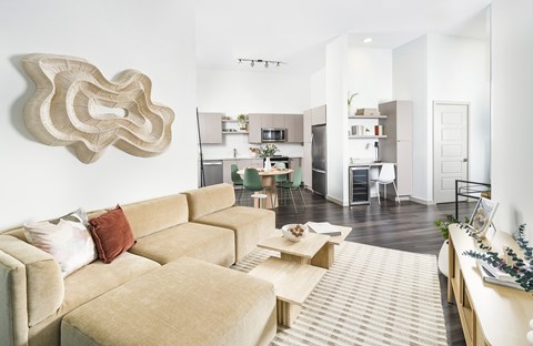 A living room with a tan couch and a large sculpture on the wall.