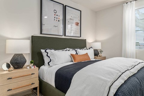 A bedroom with a large bed, a nightstand with a lamp, and two framed pictures on the wall.