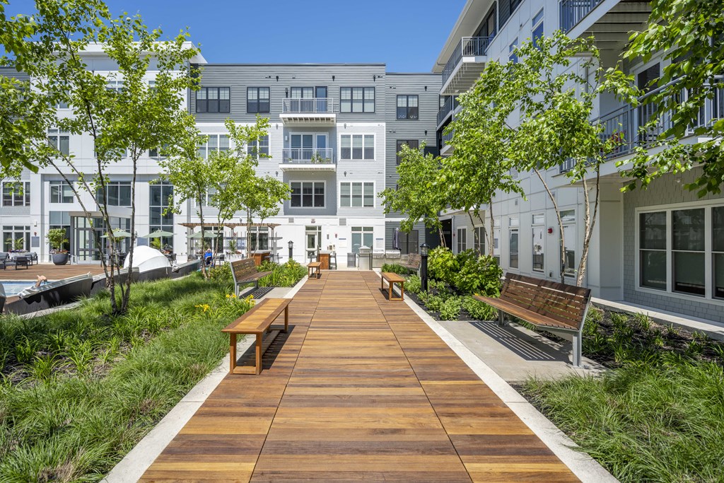 a boardwalk with benches and trees in front of apartments for rent at The Cove in Hingham