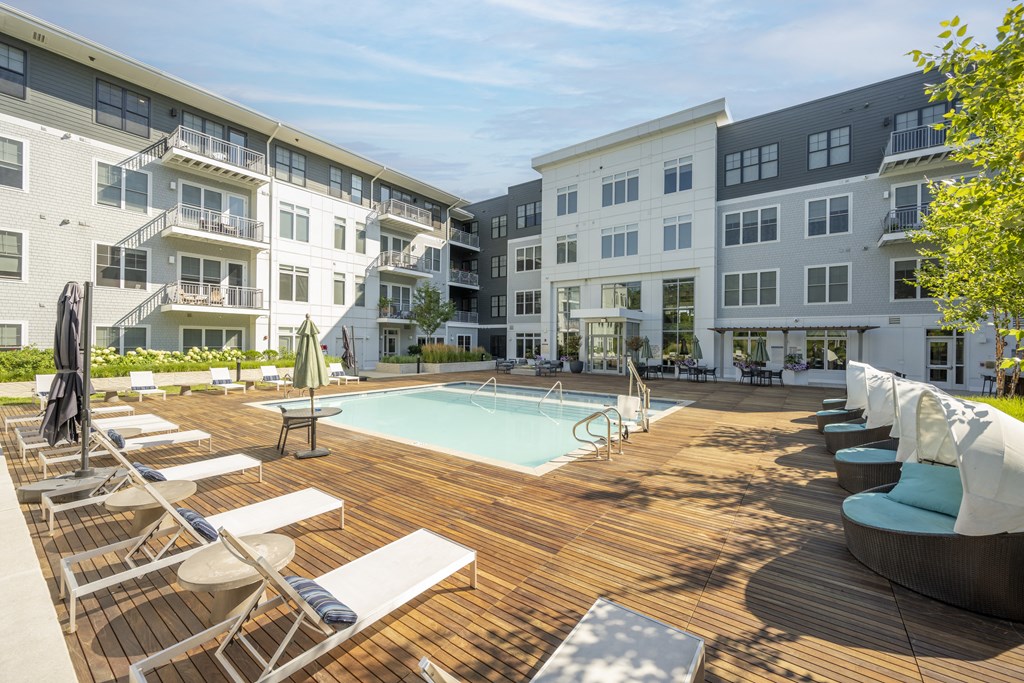 a swimming pool with lounge chairs and umbrellas in front of an apartment building