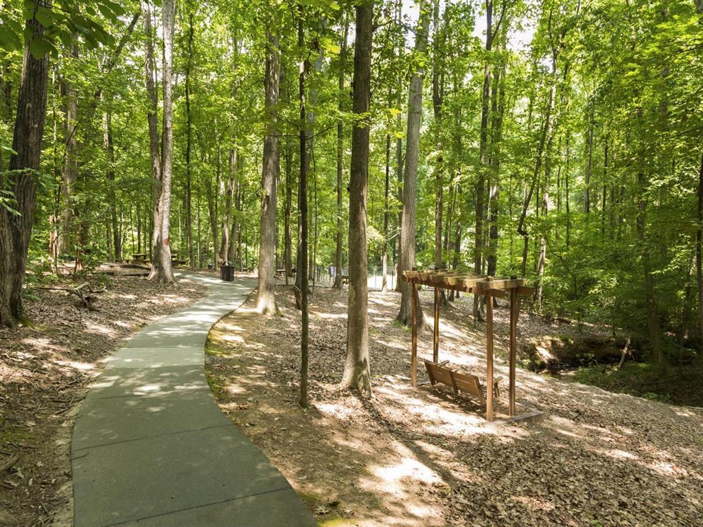 a paved path in the woods with trees and a sign