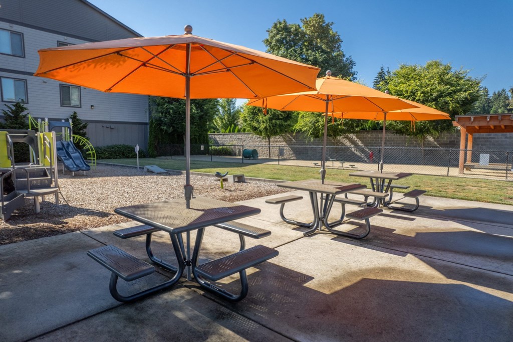 two orange umbrellas and picnic tables in a park