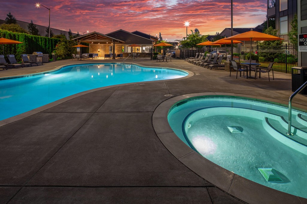 a swimming pool at dusk with umbrellas and a building in the background