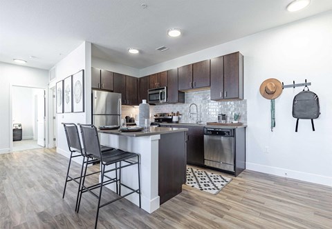a kitchen with dark wood cabinets and a white island with three stools at RockVue, Broomfield, CO, 80021