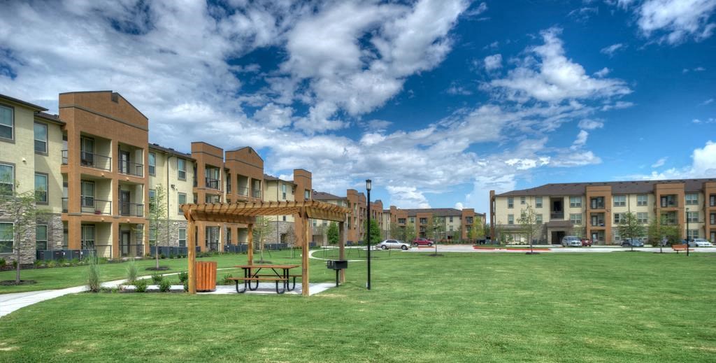 a picnic area in the middle of a grassy area with buildings in the background