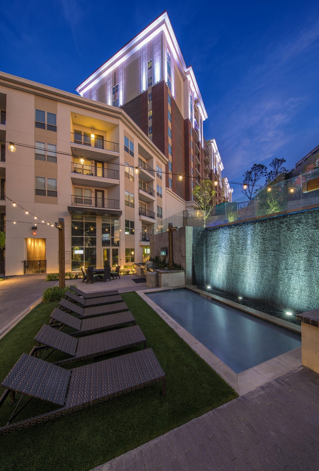 A modern building with a pool and lounge chairs.