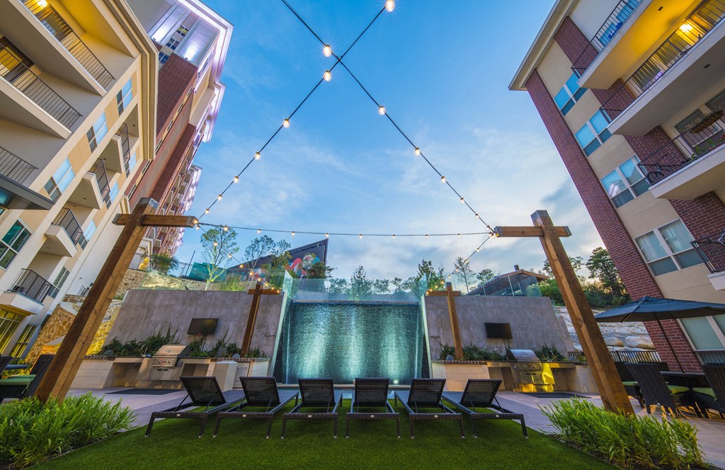 A modern outdoor seating area with a water feature and string lights.