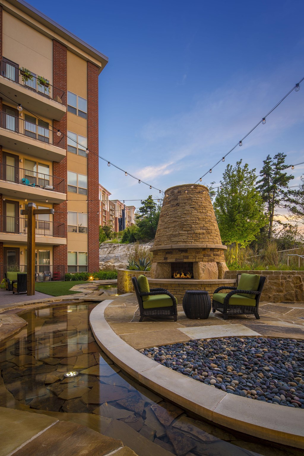 A modern outdoor seating area with a stone fireplace and a pond.