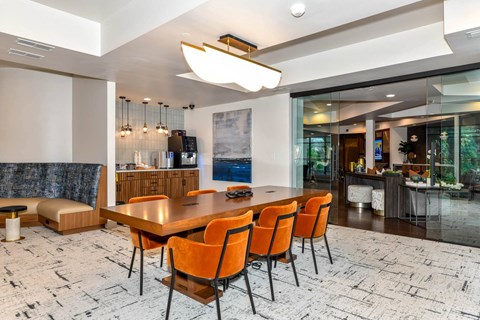 A modern dining room with a large table and orange chairs.