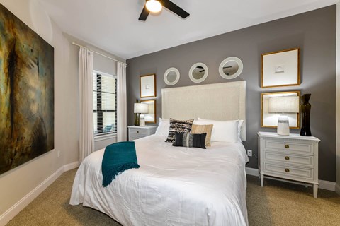 A bedroom with a large bed, a ceiling fan, and a painting on the wall.