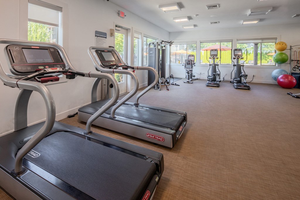 a gym with treadmills and other exercise equipment in a building with windows