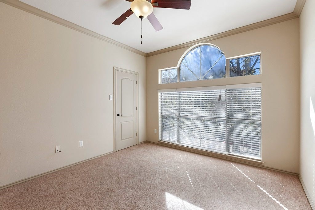 an empty living room with a large window and a ceiling fan