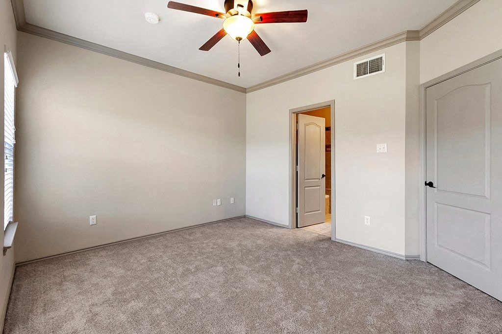 an empty living room with a ceiling fan and a door to a hallway