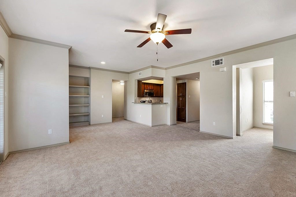 an empty living room with a ceiling fan and a kitchen