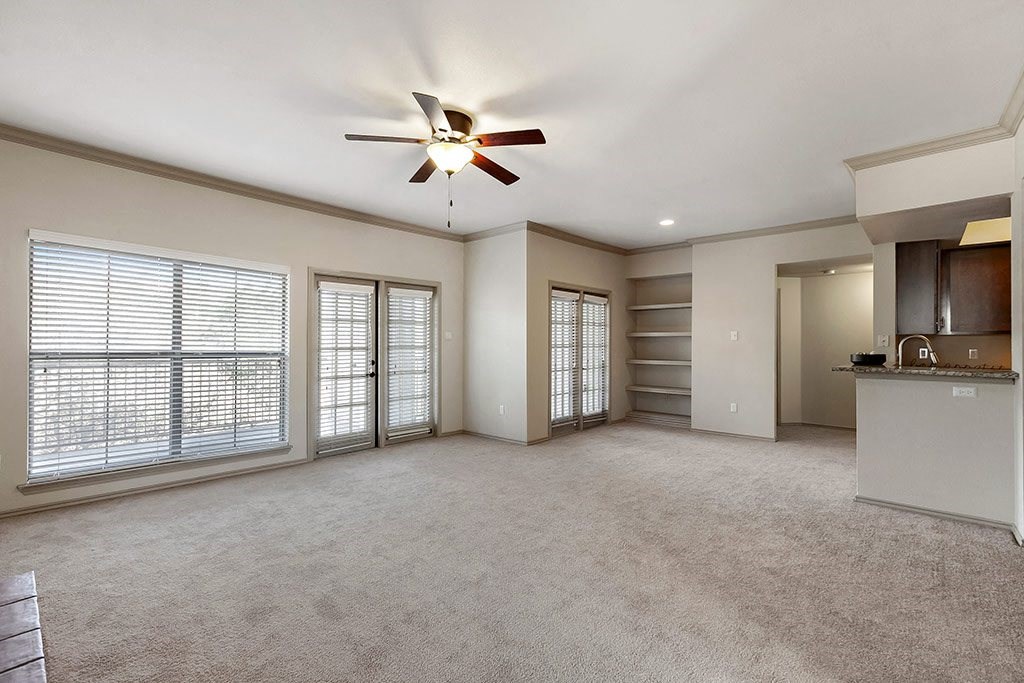 an empty living room with a ceiling fan and windows