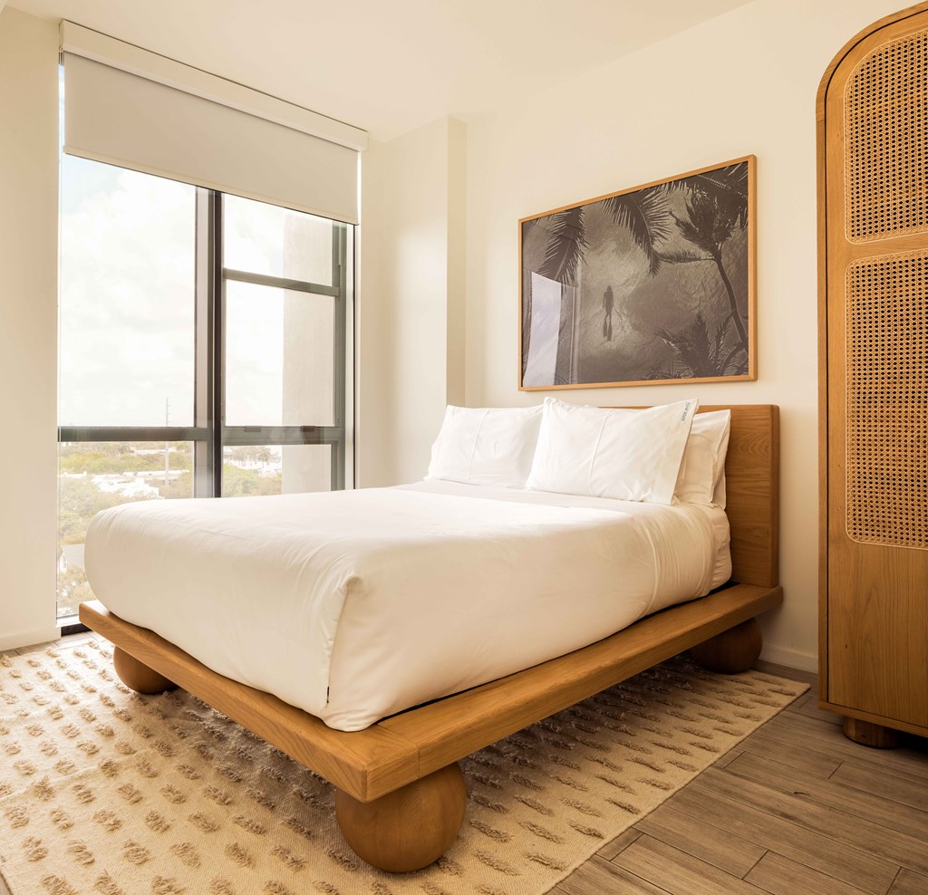 A bed with white sheets and a wooden headboard sits in a room with a large window.