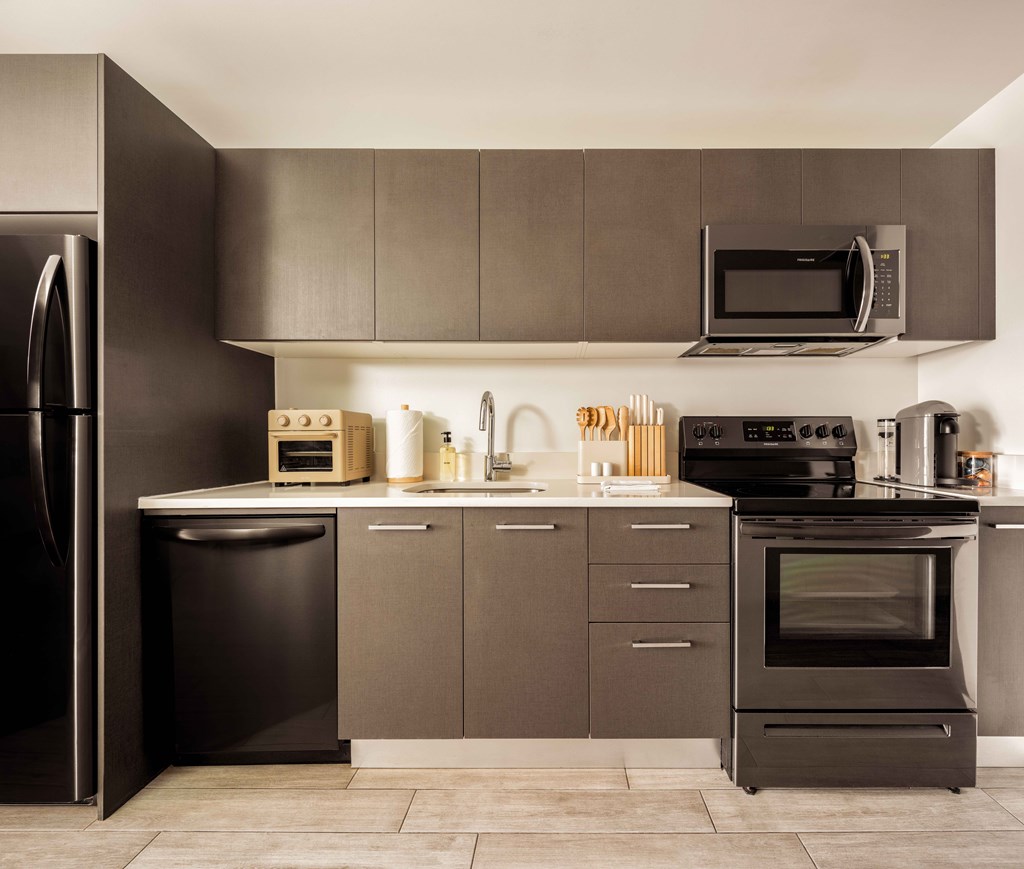A modern kitchen with a black refrigerator, microwave, oven, and sink.