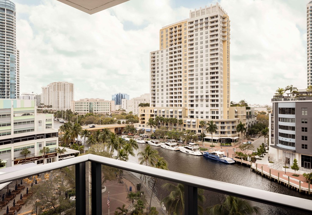 A view of a cityscape from a balcony with buildings, boats, and palm trees.