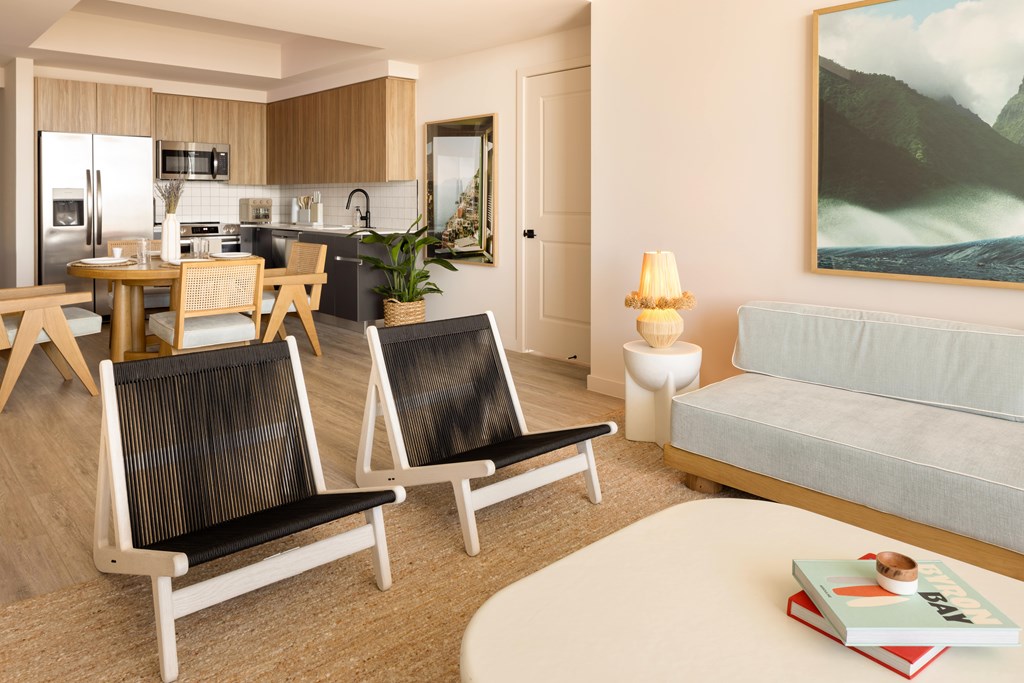 A living room with a grey sofa, a dining table with chairs, a coffee table, and a painting on the wall.