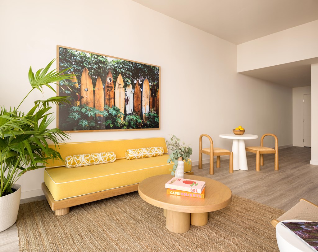 A living room with a yellow sofa and a painting of a village scene on the wall.