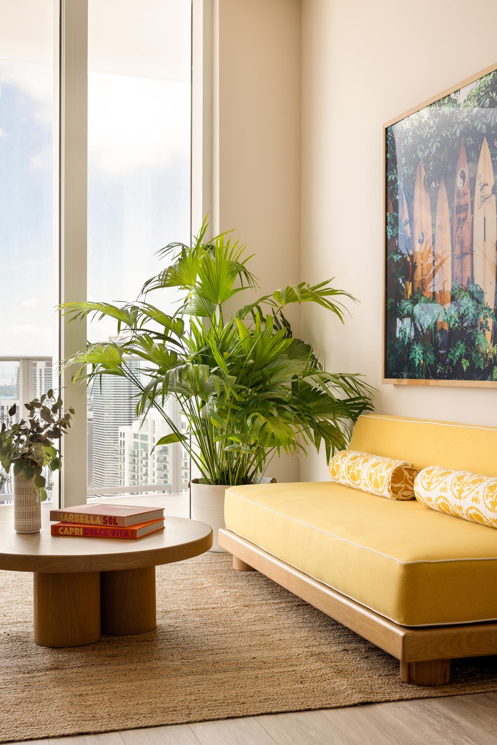 A living room with a yellow couch, a round table, and a painting on the wall.