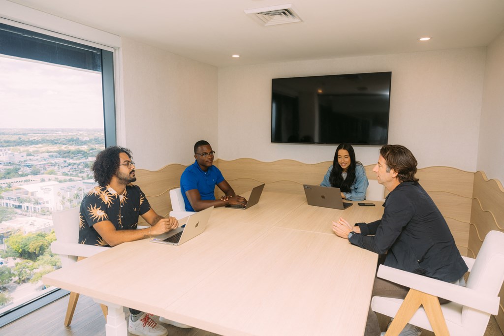 a group of people sitting around a table with laptops