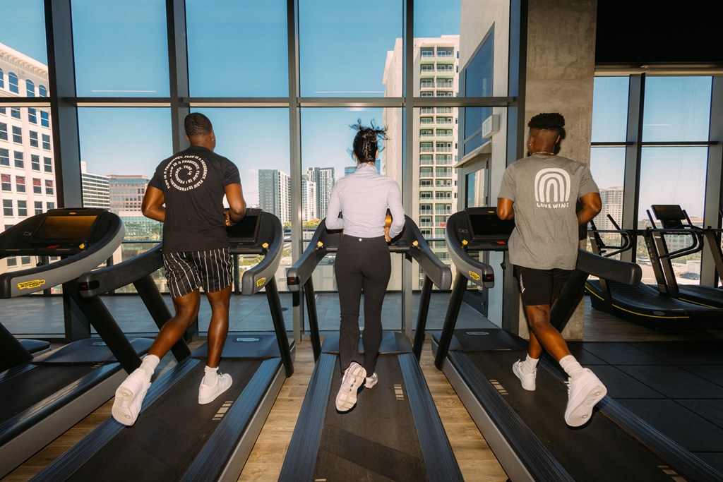 three people running on treadmills in front of a window at a gym